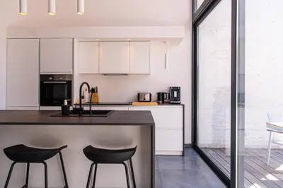 a kitchen with white cabinets and black bar stools at Garden Guillemins Station in Liège