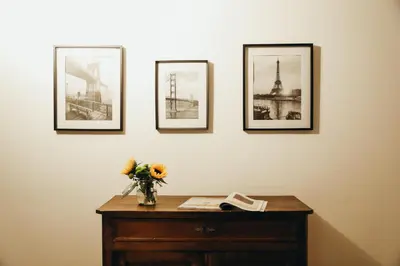a table with a vase of flowers and four pictures on a wall at L'Orée du Bois by WelcHome in Verviers