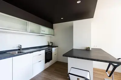 a kitchen with white cabinets and a black counter top at Appart'hotel Urban Lodge in Chaudfontaine