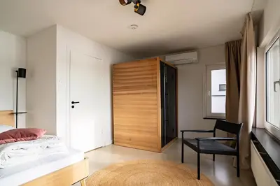 a bedroom with a bed and a chair and a door at Maas Suites - The River House with private sauna in Lanaken