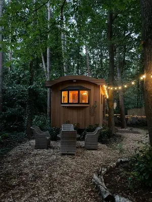 a small cabin in the woods with chairs and lights at Pipowagen de Pauw in de bossen van Belgisch Limburg nabij Maastricht in Lanaken