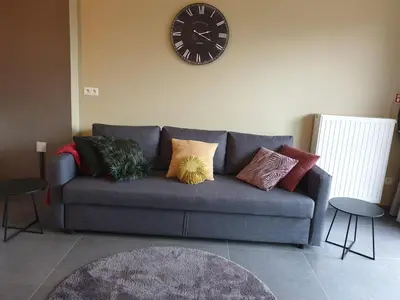 a blue couch with pillows and a clock on the wall at Het Zonnetje -Vakantiewoning en Bed and Breakfast in Dilsen-Stokkem