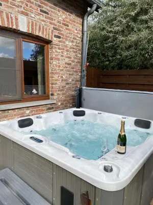 a hot tub with a bottle and a wine glass in it at Le Logis du Plateau in Herve