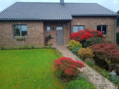 a brick house with red flowers in the yard at Le Logis du Plateau in Herve