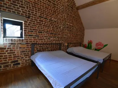 two beds in a room with a brick wall at Teuven Farmhouse for 24 Guests in Teuven