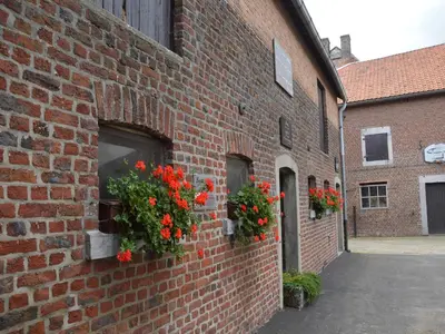 a brick building with two flowerpots with red flowers at Teuven Farmhouse for 24 Guests in Teuven