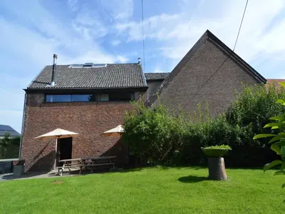 a brick house with two tables and two umbrellas at Teuven Farmhouse for 24 Guests in Teuven