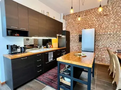 a kitchen with black cabinets and a brick wall at Art Loft -Opéra, Saint-Lambert, Bueren in Liège
