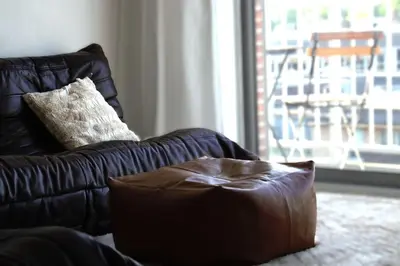a brown leather couch with a pillow and a window at Stijlvol App in Genk Centrum in Genk