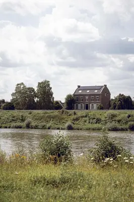 a house on top of a hill next to a river at Het Maashuis in Maasmechelen