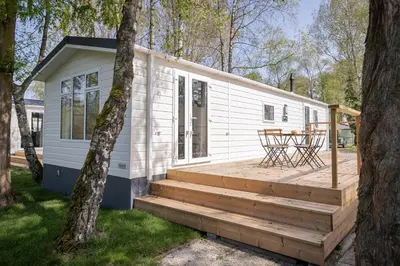 a small white tiny house with a wooden deck at Vakantiehuis Hoge Kempen - 25 minuten Roermond, Maasmechelen & Maastricht in Kinrooi