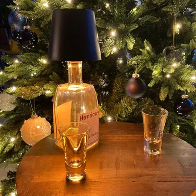 a bottle of alcohol and two glasses on a table with a christmas tree at DeStoker in Hasselt