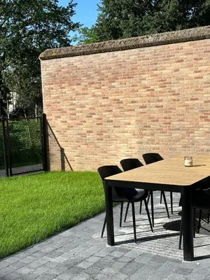 a wooden table and chairs next to a brick wall at Vakantie aan de Maas - Vakantiewoning Leenhof in Kinrooi