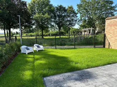 two white chairs sitting in the grass near a fence at Vakantie aan de Maas - Vakantiewoning Leenhof in Kinrooi