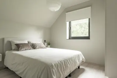 a white bedroom with a white bed and a window at Vakantie aan de Maas - Vakantiewoning Neerhof in Kinrooi
