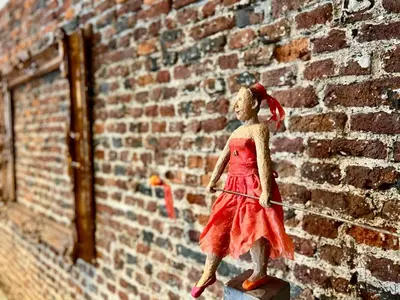 a toy doll in a red dress standing next to a brick wall at La maison de Maître - Grand Jardin, Face à la Meuse in Hermalle-sous-Argenteau