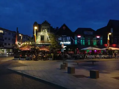 a town square at night with people sitting at tables at De Brugdraaier - The Bridge Turner in Neerpelt