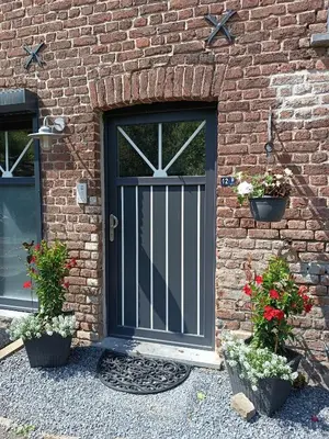 a black door on a brick wall with two potted plants at B&B Ferme du Petit Breuil in Verviers