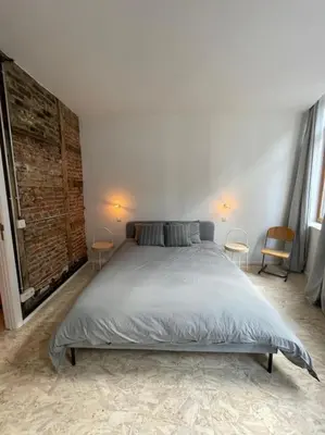 a bedroom with a bed with two chairs and two windows at 2 bedroom duplex in the historic heart of Liège in Liège