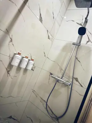 a white tiled bathroom with a shower with two buckets at Appartement cosy à Liège in Liège