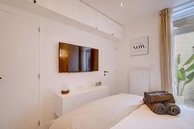 a white bedroom with a bed and a tv on the wall at - Suite Solvay - Cosy & Modern Flat in Liège