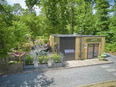 a tiny house in the woods with a person sitting on a porch at Zen en Zoet in Zutendaal
