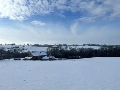 a field covered in snow with a barn in the background at La Bushaye in Aubel
