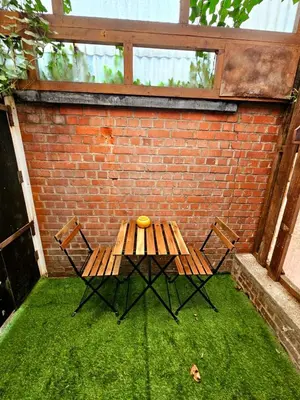 a wooden table and two chairs in front of a brick wall at Jolie petite maison in Liège