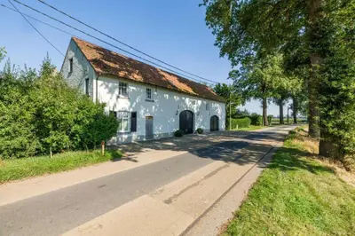 a white building with a rusty roof on the side of a road at Vakantiewoning Molenveld in Dilsen-Stokkem