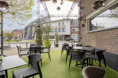 a patio with tables and chairs and a building at Hotel De Boskar Pelt in Pelt