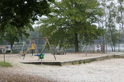 a playground in a park with a bench and swings at De Onthaasting in Lanaken