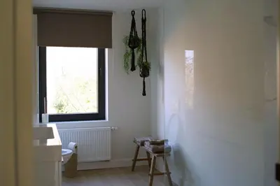 a white bathroom with a window and a stool at Maison Magnifiek in Hasselt