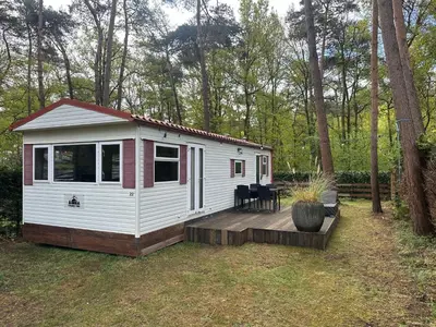 a small white cabin with a deck in a yard at Chalet Tibi in Bocholt