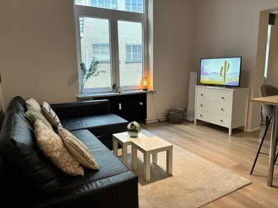 a living room with a black couch and a tv at Le coeur Liégeois - Hypercentre quartier piéton in Liège