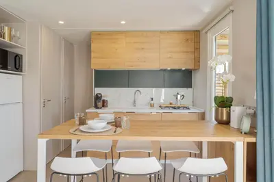 a kitchen with a wooden island with white chairs at Holiday home La Casetta in Kinrooi