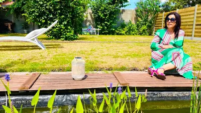a woman sitting on a wooden boardwalk next to a pond at BEEEP Stay in Hasselt