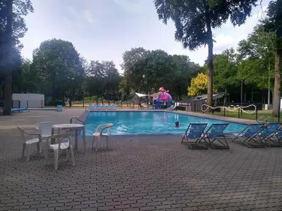 a pool with chairs and a table and a person in the background at Studio Eik 105 at the pool in nature domain in Houthalen-Helchteren