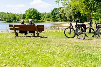 two people sitting on a park bench near a lake at Boshuisje met jacuzzi in Lanaken