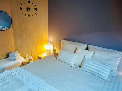 a bed with white pillows and a clock on the wall at Appartement rustique à Liège in Liège