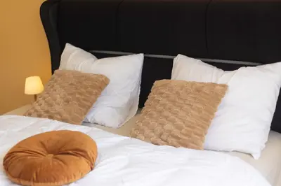 a bed with white pillows and a brown pillow on it at Appartement de luxe Dubai , Chambre, salon et SDB Privés, cuisine partagée in Liège