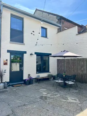 a patio with a table and an umbrella in front of a house at La maison de MiLy in Bassenge