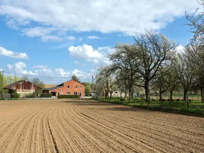 a plowed field in front of a red barn at Cozy duplex apartment with terrace in Heers