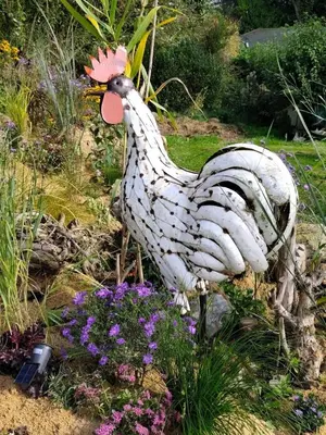 a statue of a chicken standing in some flowers at Tiny House Dreiländereck in La Calamine