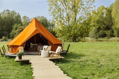 an orange tent with chairs and a boardwalk in a field at Glamping Chateau d'Hamont in Herk-de-Stad