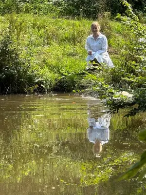 a woman sitting next to a body of water at Homestorys Nature Resort - Wood Lounge in Eupen