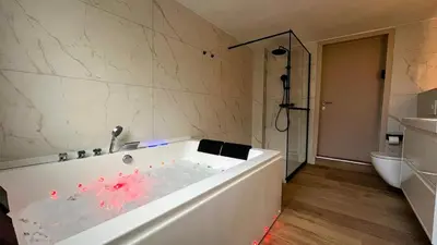 a white bath tub in a bathroom with a toilet at Chez Margueritte, Cosy, Jacuzzi & Parking Facile in Liège