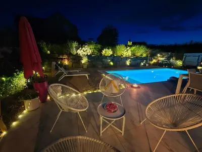 a patio with chairs and a pool at night at Villa Marvin in Soumagne
