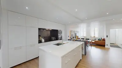 a kitchen with white cabinets and a living room at Home cinema in Liège