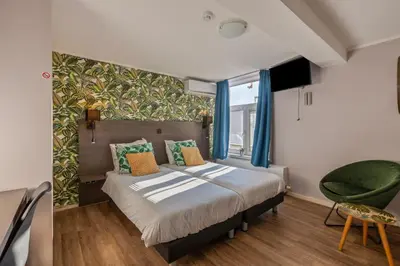 a bedroom with a bed and a green chair at Hotel Brasserie de Klok in Zutendaal