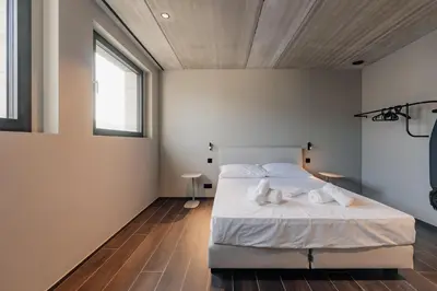 a bedroom with a bed with white sheets and two windows at Coliving - Bord de Meuse - L'écrin Vert in Oupeye